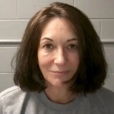 Ghislaine Maxwell wearing a gray T-shirt, standing in front of a white wall.