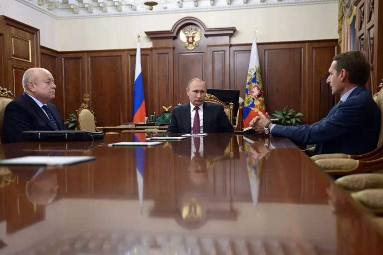 Vladimir Putin sits at a meeting table alongside Sergey Naryshkin and Mikhail Fradkov during a formal Kremlin discussion.