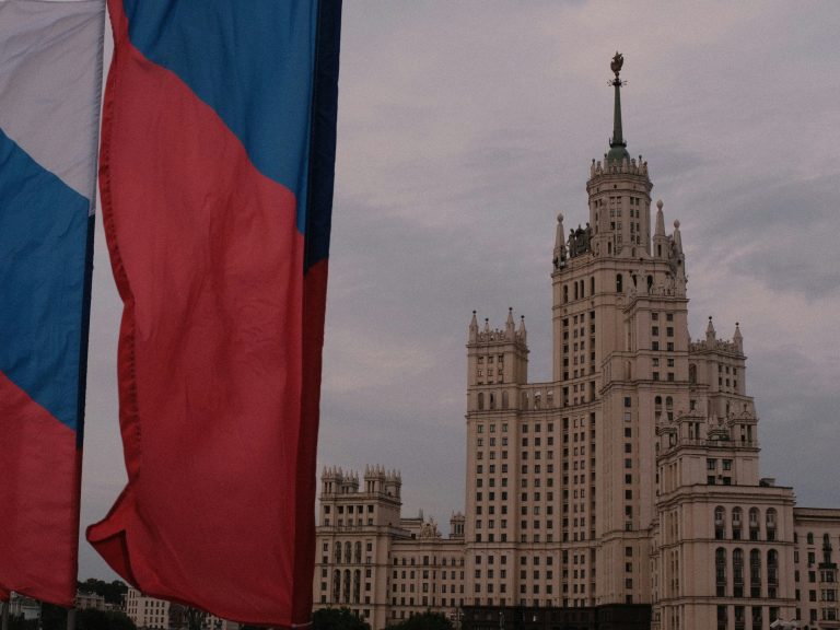 Close-up of Russian flags waving in front of a large government building.