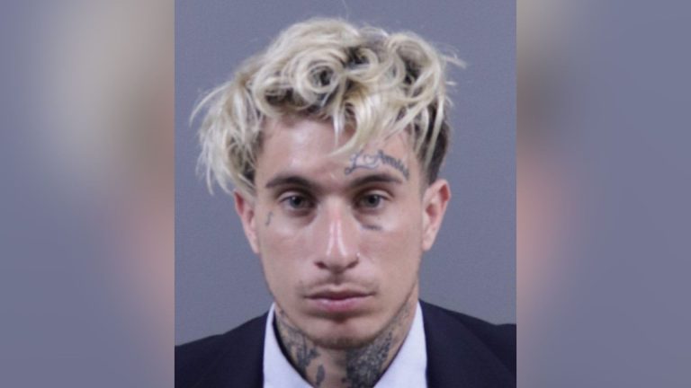 Mugshot of Brandon Holguin, a 26-year-old man with dyed blonde hair and facial tattoos.