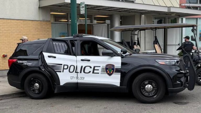A Lodi Police Department patrol SUV parked along a city street in California near commercial buildings and officers.